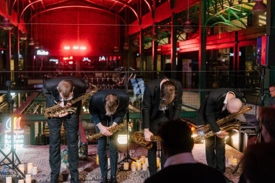 Miniature DJ Saint-Gilles (Bruxelles-Capitale) - 441 Quartet #4 Quatre hommes en costume posant debout dans un espace lumineux avec des colonnes en arrière-plan.