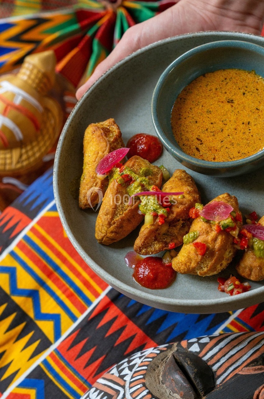 Assiette de beignets dorés accompagnés de sauces colorées, présentée sur un tissu aux motifs africains.