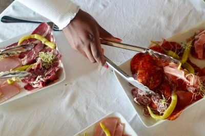 Une main sert de la charcuterie variée sur une table dressée avec des assiettes de viandes froides et de garnitures.