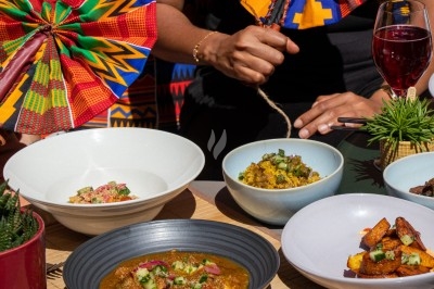 Repas coloré avec plats variés dans des bols, accompagné de boissons, sur une table décorée de motifs africains.