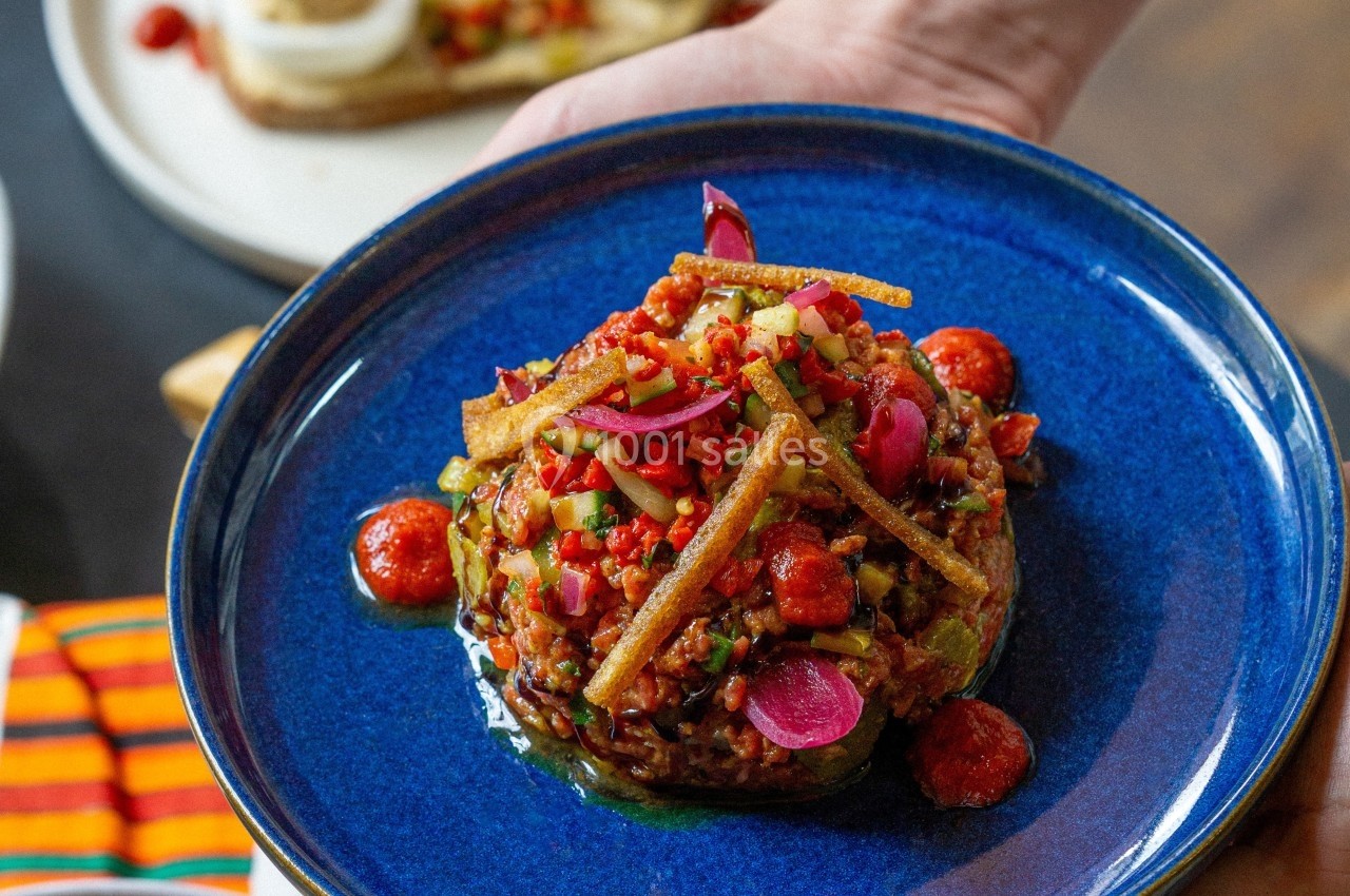 Plat coloré composé de légumes, condiments et garnitures croustillantes, présenté sur une assiette bleue.