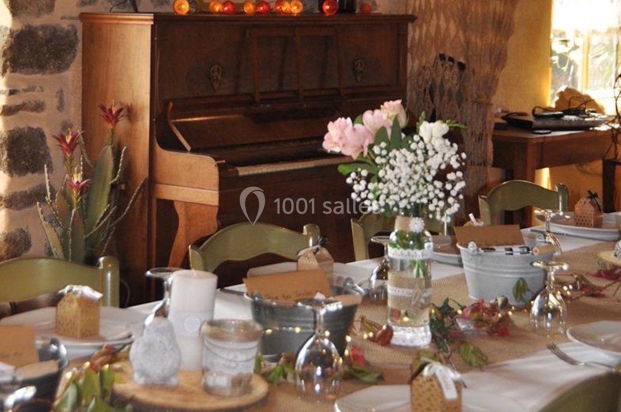 Table décorée pour un repas, avec fleurs, petits cadeaux et un piano en arrière-plan dans une pièce rustique.