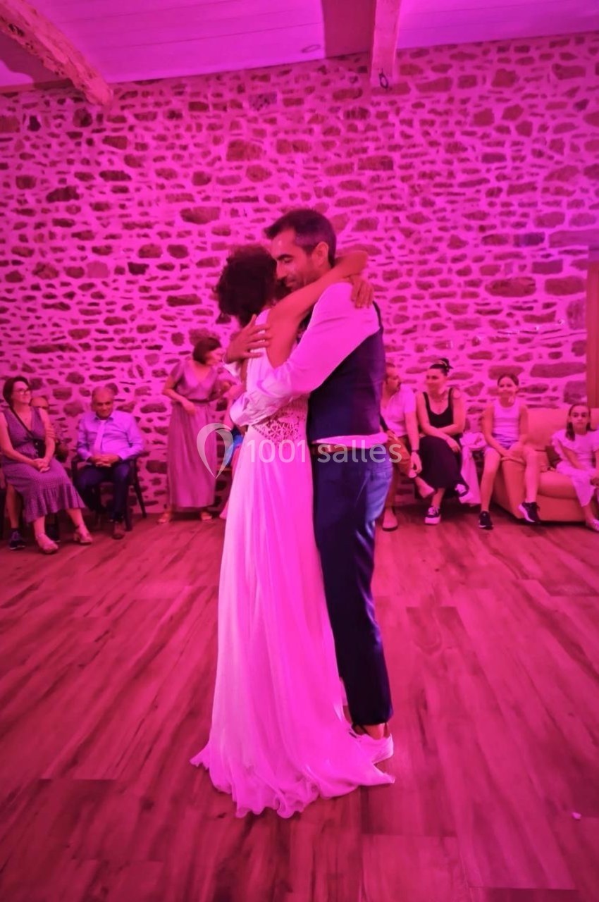 Un couple s'enlace sur une piste de danse éclairée par une lumière rose, entouré de spectateurs assis.