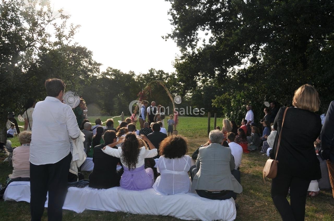 Groupe de personnes assises en extérieur, assistant à une cérémonie dans un cadre verdoyant et ensoleillé.