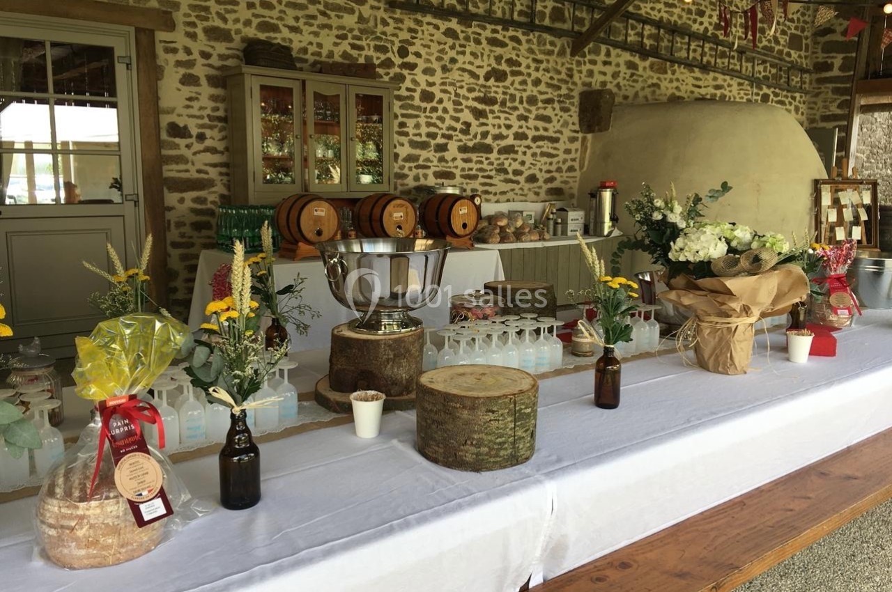 Table décorée avec des fleurs, des boissons, des produits locaux et des tonneaux dans un cadre rustique en pierre.