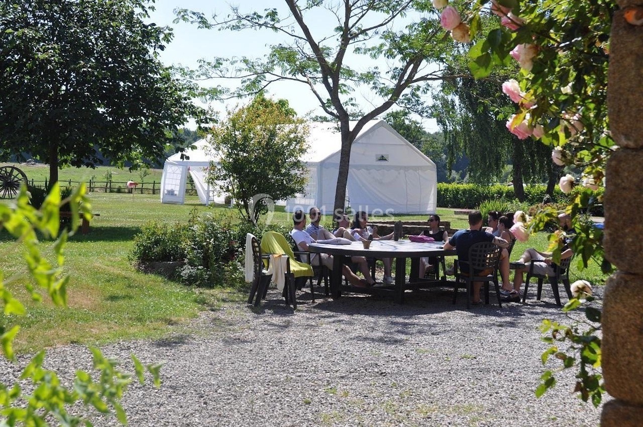 Groupe de personnes assises autour d'une table en plein air, près de tentes blanches dans un jardin verdoyant.