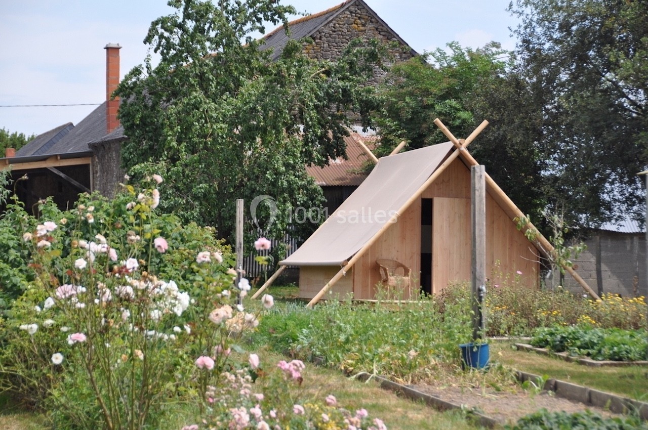 Abri en bois avec toit incliné dans un jardin fleuri, entouré d'arbres et de végétation.