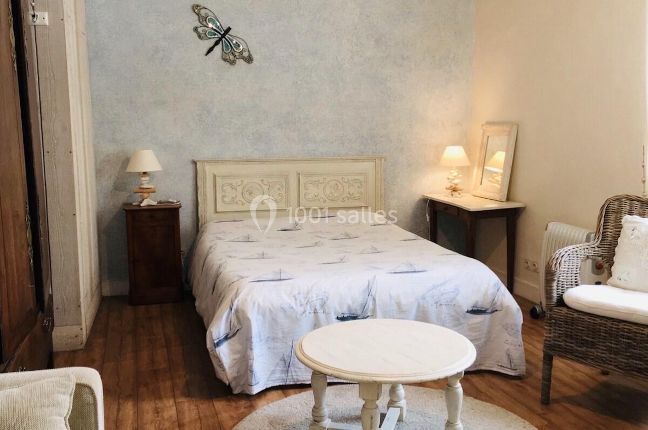 Chambre lumineuse avec lit double, table basse ronde, fauteuil en osier et décoration murale en forme de papillon.