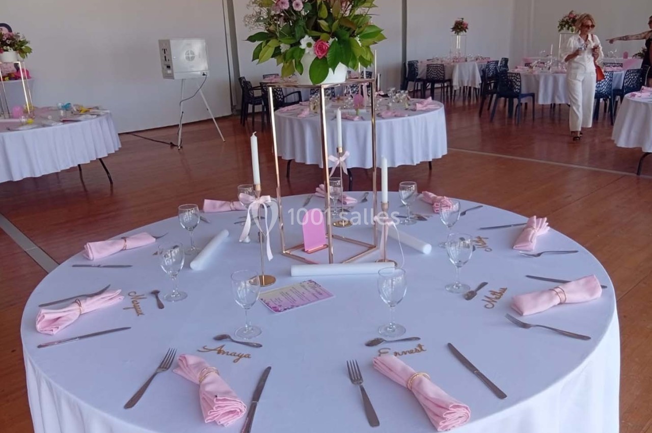 Table ronde décorée pour un événement, avec nappes blanches, serviettes roses, bougies et centre de table fleuri.