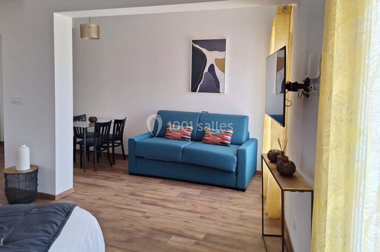 Salon lumineux avec canapé bleu, table à manger en bois, rideaux jaunes et décoration murale abstraite.