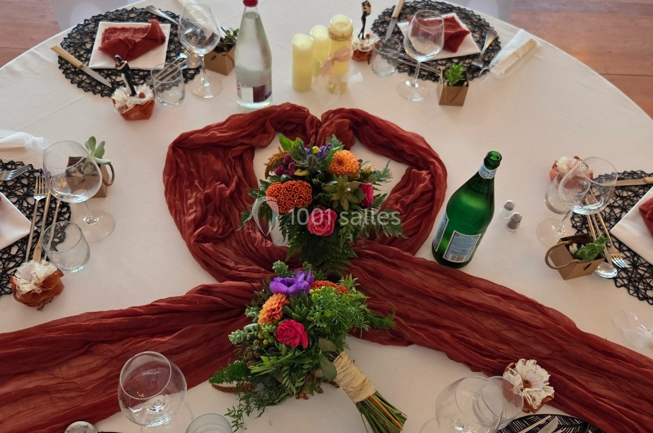 Table dressée avec nappes blanches, décorations florales colorées, serviettes pliées et bouteilles d'eau.