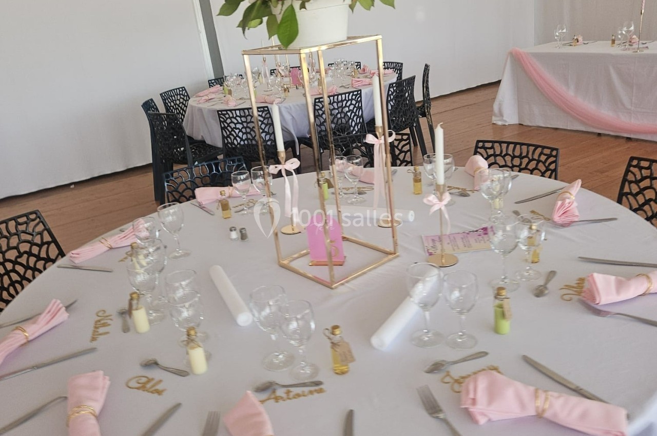 Table ronde décorée pour un événement, avec nappes blanches, serviettes roses, bougies et centre de table élégant.