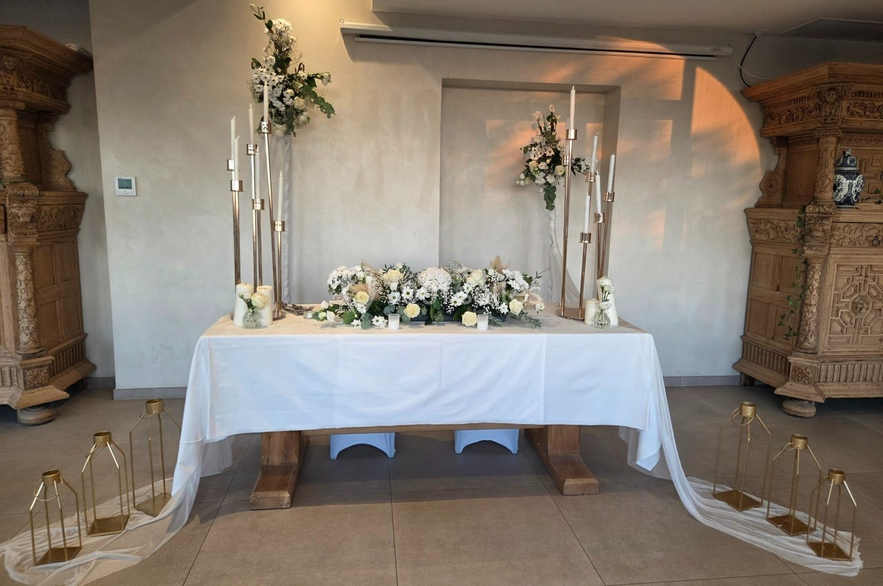 Table décorée pour un mariage avec fleurs blanches, chandeliers dorés et voilages, dans une salle lumineuse au style…