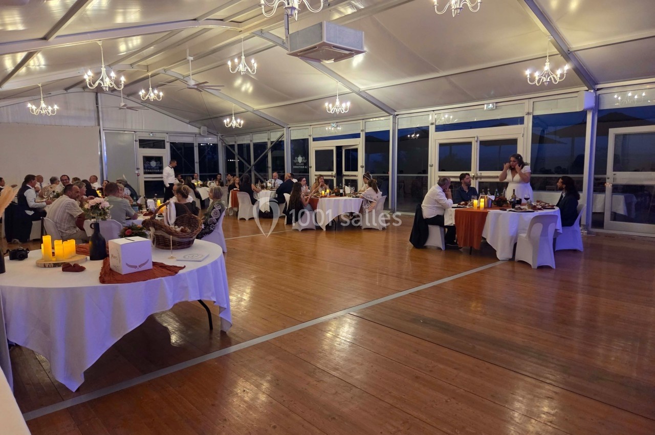 Salle de réception éclairée avec des convives assis à des tables rondes, décorée de chandeliers et bougies.