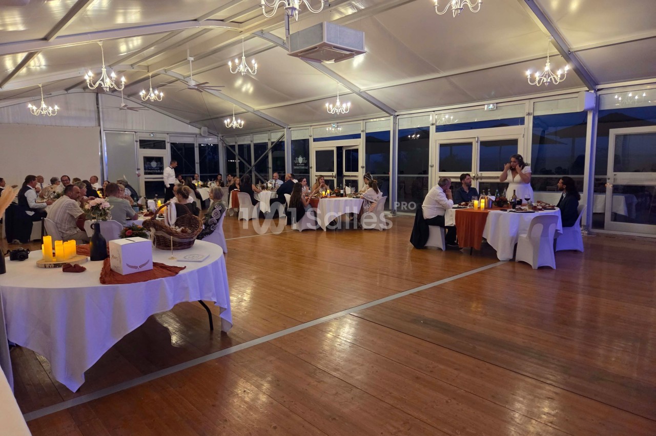 Salle de réception éclairée avec des convives assis à des tables rondes, décorée de chandeliers et bougies.