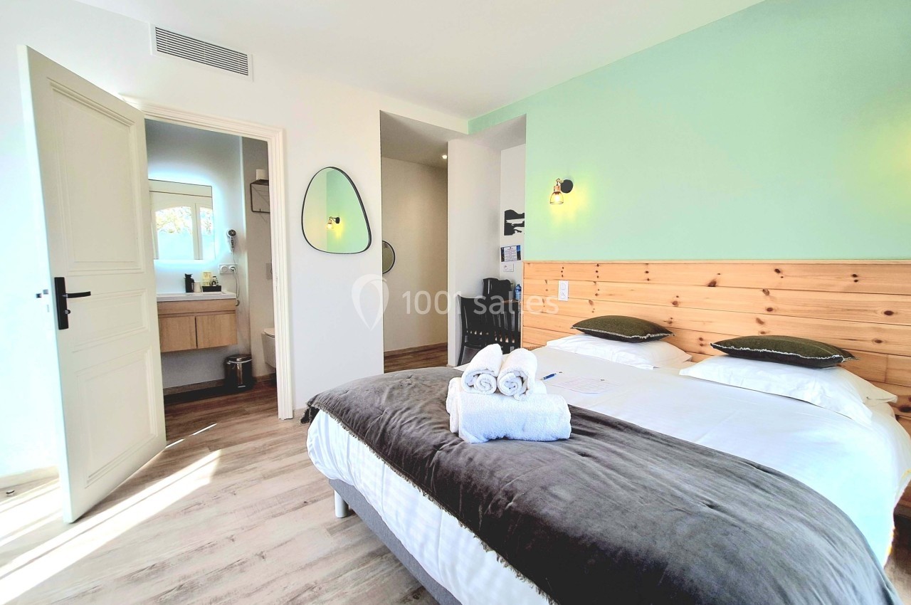 Chambre lumineuse avec lit double, tête de lit en bois, salle de bain attenante et décoration moderne.