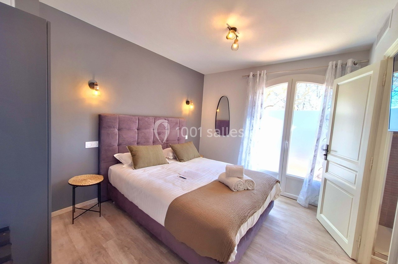 Chambre lumineuse avec lit double, murs gris, éclairages muraux, fenêtre avec rideaux et table d'appoint.