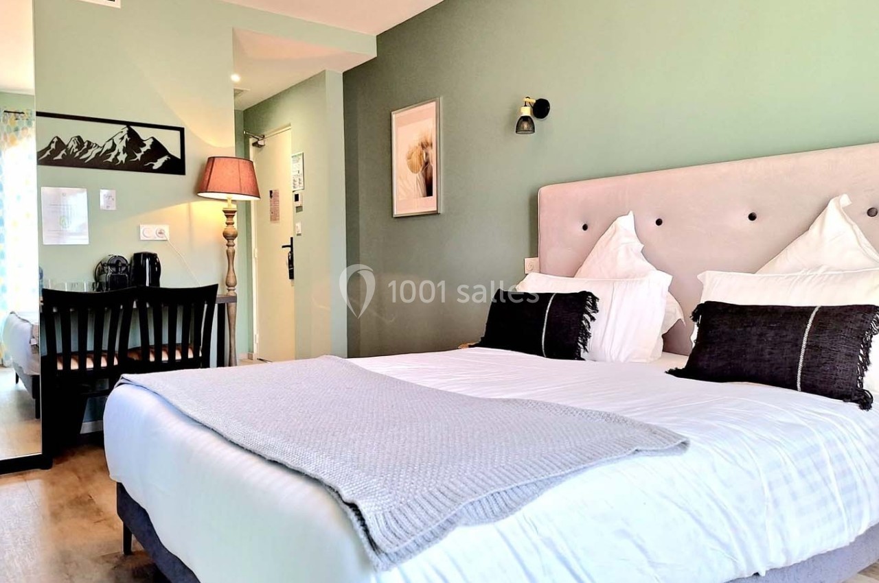 Chambre lumineuse avec lit double, tête de lit rembourrée, bureau, miroir et mur peint en vert pastel.