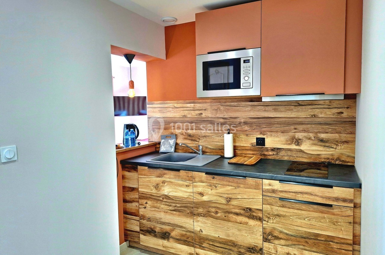 Cuisine moderne avec meubles en bois, plan de travail sombre, évier, micro-ondes intégré et éclairage suspendu.