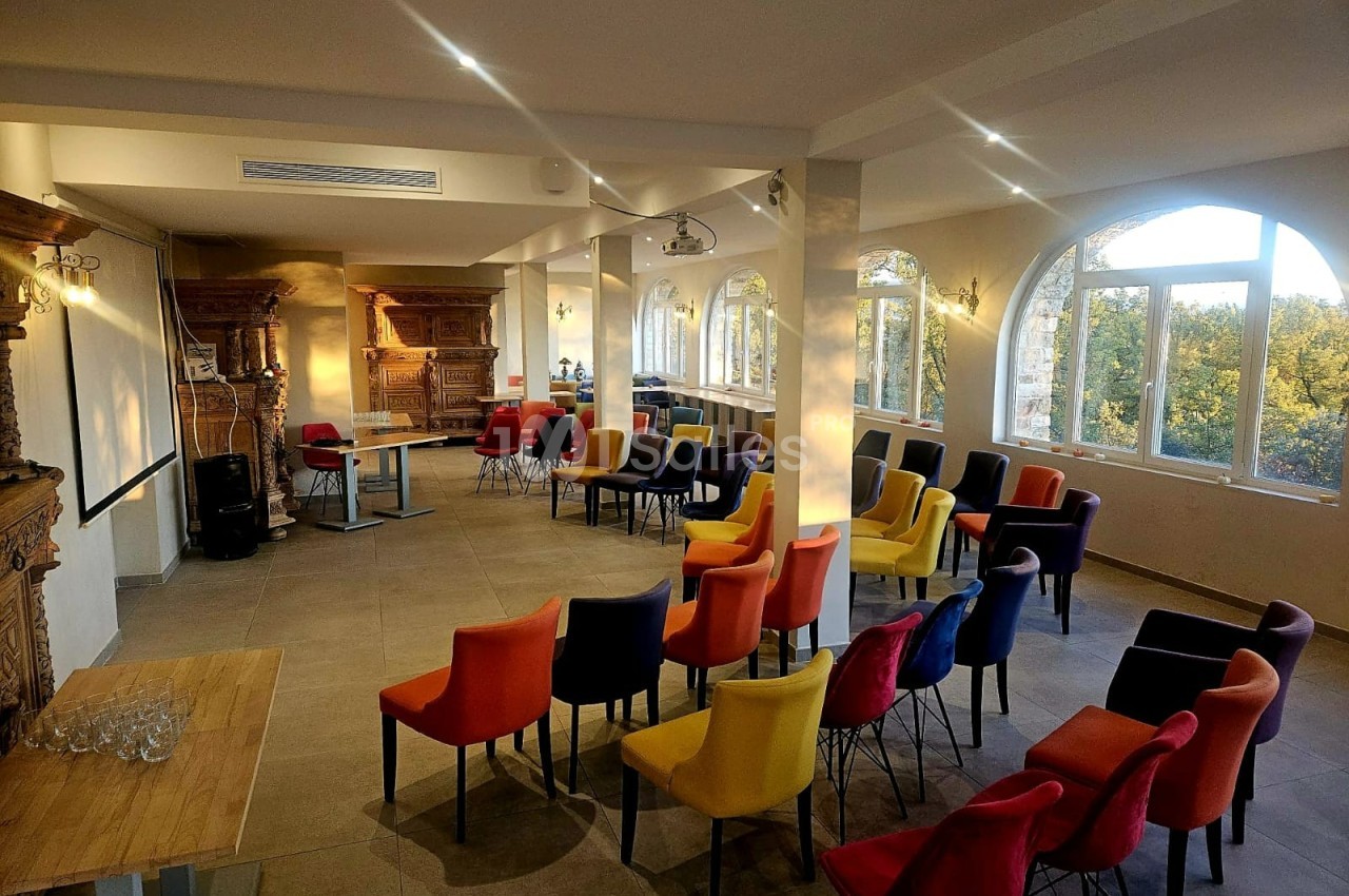 Salle lumineuse aménagée pour une conférence, avec des chaises colorées disposées face à un espace de présentation.