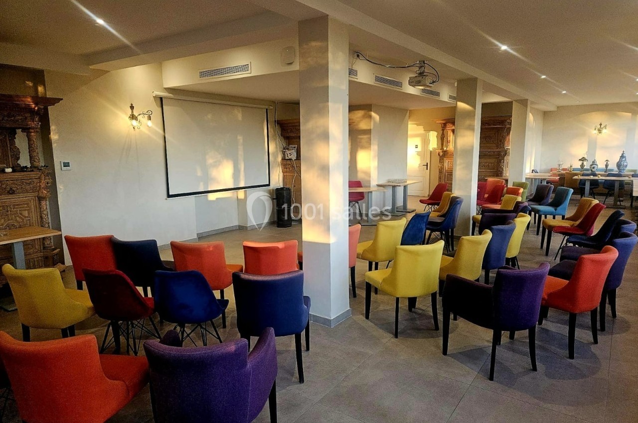 Salle de réunion lumineuse avec des rangées de chaises colorées disposées face à un écran de projection.