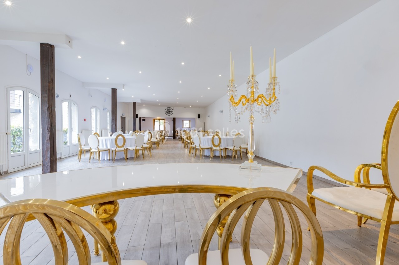 Salle de réception lumineuse avec tables et chaises blanches et dorées, décorée d'un chandelier élégant au premier plan.