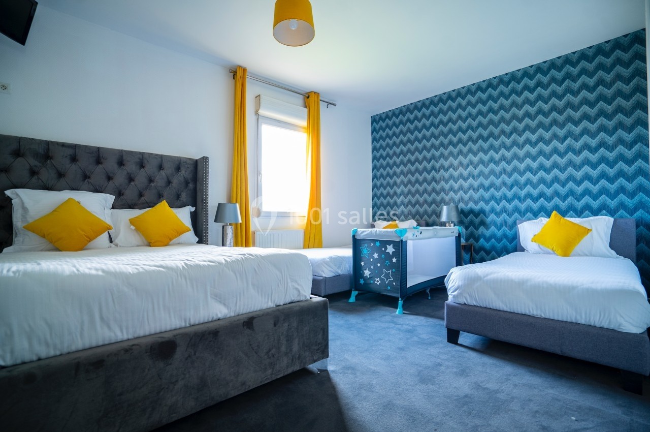 Chambre lumineuse avec deux lits simples, un lit double, un berceau et des rideaux jaunes, décorée de motifs bleus.