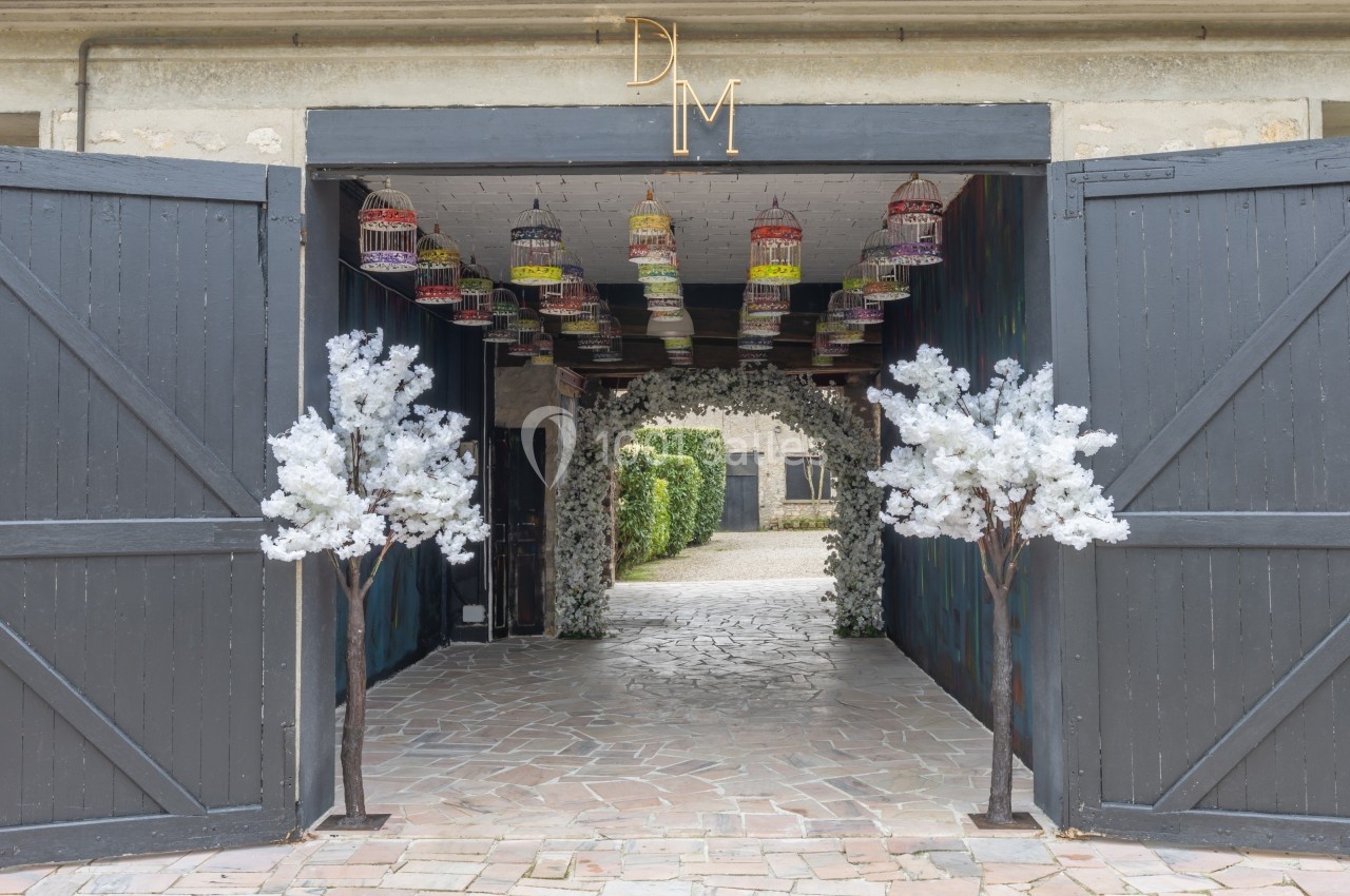 Entrée décorée avec des portes en bois ouvertes, des arbres artificiels blancs et des cages suspendues colorées.