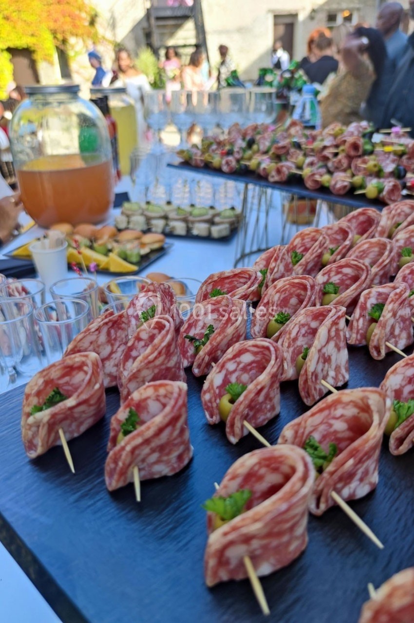 Plateau de charcuterie avec tranches de saucisson enroulées sur des piques, accompagné de boissons et autres amuse-bouches.
