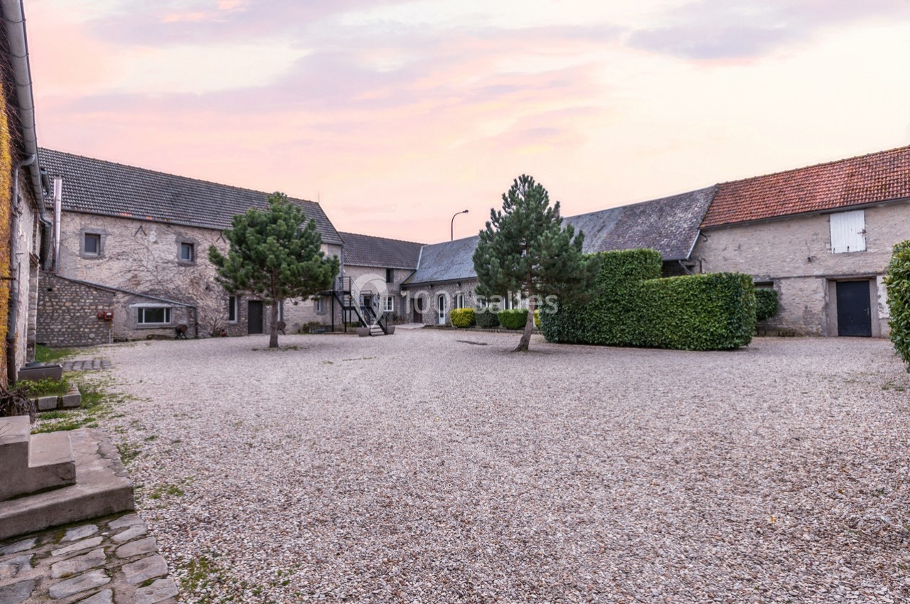 Cour pavée entourée de bâtiments en pierre et en briques, avec des arbres et un ciel rose en arrière-plan.