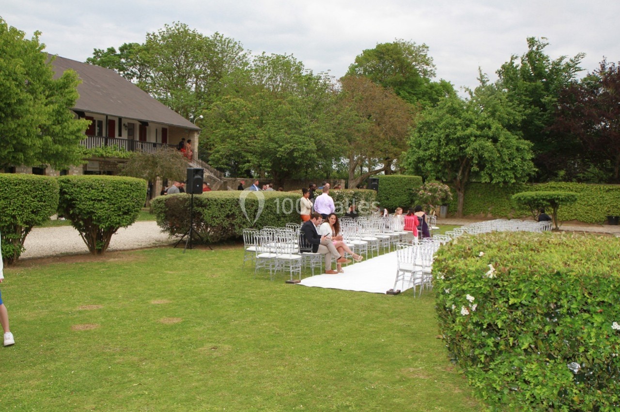 Chaises transparentes disposées sur une pelouse autour d'une allée blanche, préparées pour une cérémonie en extérieur.