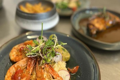 Assiette de crevettes grillées servies avec légumes et herbes fraîches, accompagnée de plats en arrière-plan.