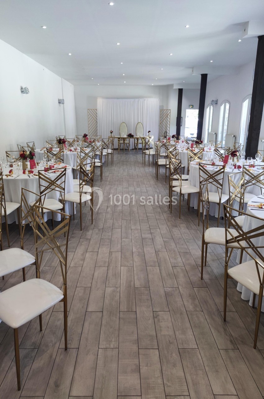 Salle de réception décorée avec des tables rondes, des chaises dorées et une table d'honneur au fond.