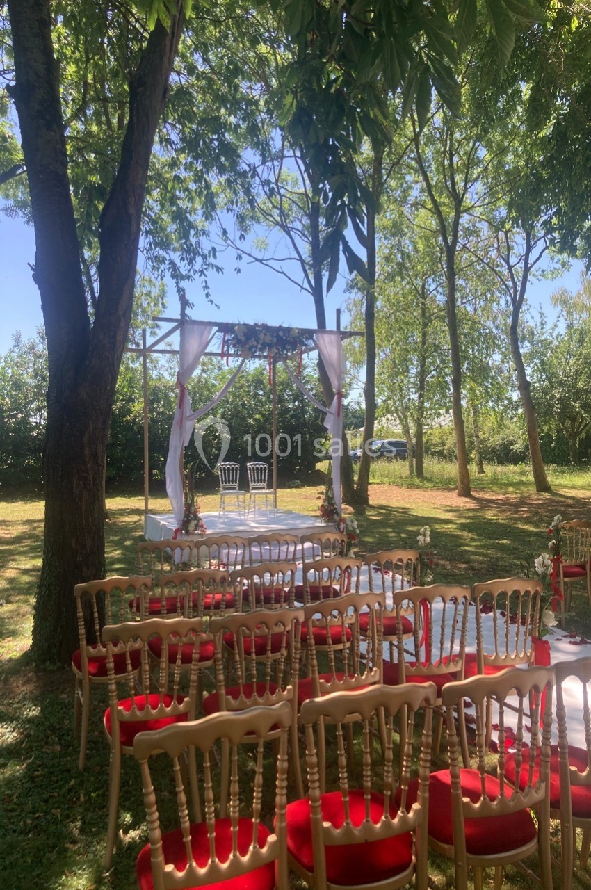 Chaises alignées devant une arche décorée de voilages blancs et de fleurs, installée dans un jardin ombragé.