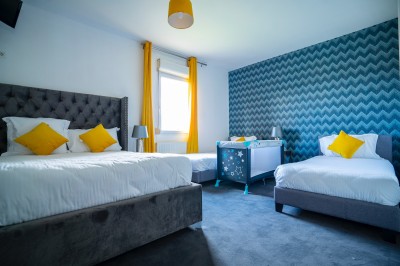 Chambre lumineuse avec deux lits simples, un lit double, un berceau et une décoration murale à motifs géométriques.