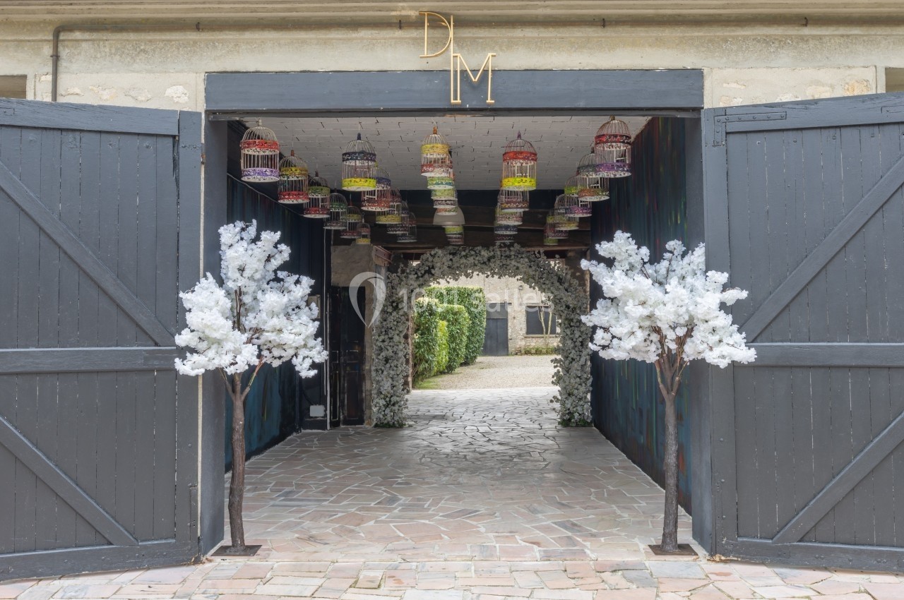 Entrée décorée avec des portes en bois ouvertes, des arbres artificiels blancs et des cages suspendues colorées.