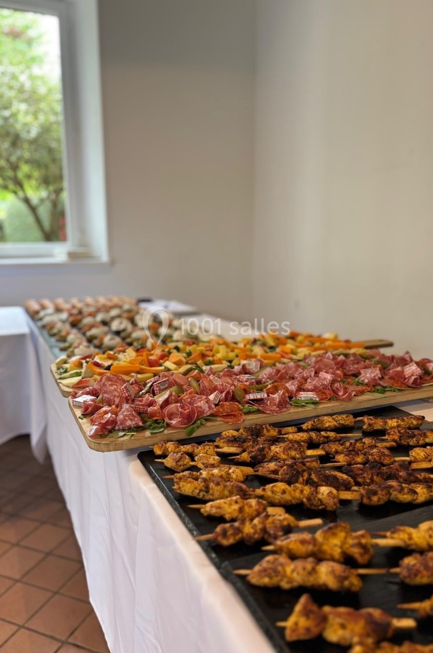 Buffet varié avec brochettes de viande, charcuterie, légumes et sushis disposés sur des plateaux dans une salle lumineuse.
