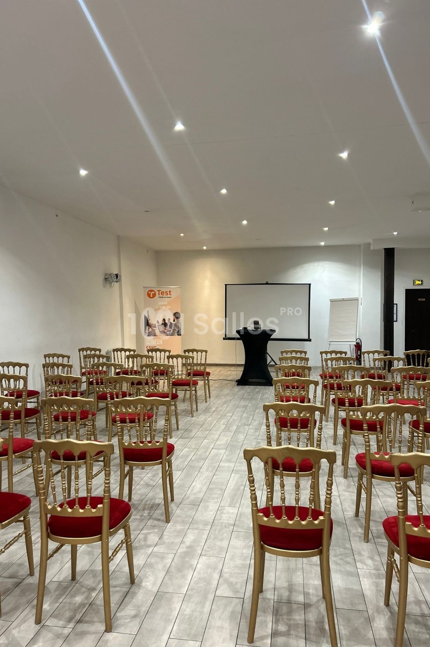 Salle de conférence lumineuse avec des chaises rouges alignées face à un écran de projection et un pupitre.