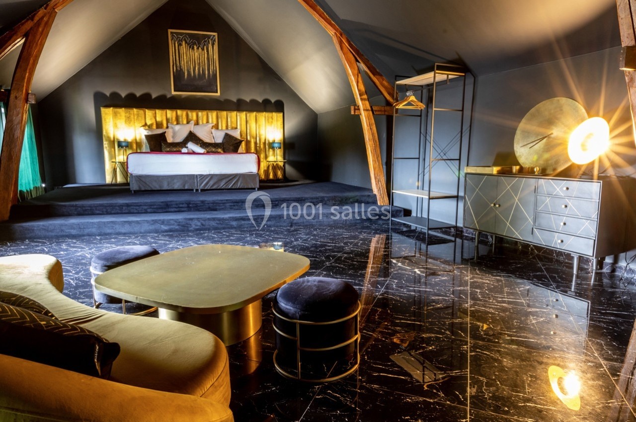 Chambre mansardée avec lit double, mobilier moderne, éclairage chaleureux et sol en marbre noir.