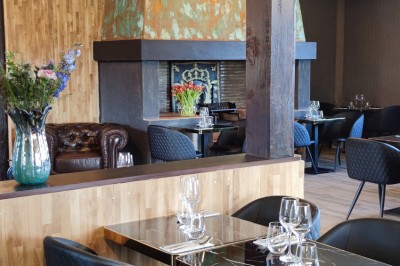 Salle de restaurant lumineuse avec tables en bois, chaises noires et décoration moderne en bois et verre.