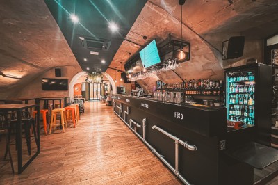 Miniature Location salle Le Mans (Sarthe) - Levrette Café le Mans #3 Intérieur d'un bar avec un long comptoir, des tabourets colorés, des étagères de boissons et un éclairage chaleureux.