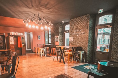 Miniature Location salle Le Mans (Sarthe) - Levrette Café le Mans #2 Intérieur d'un bar avec un long comptoir, des tabourets colorés, des étagères de boissons et un éclairage chaleureux.