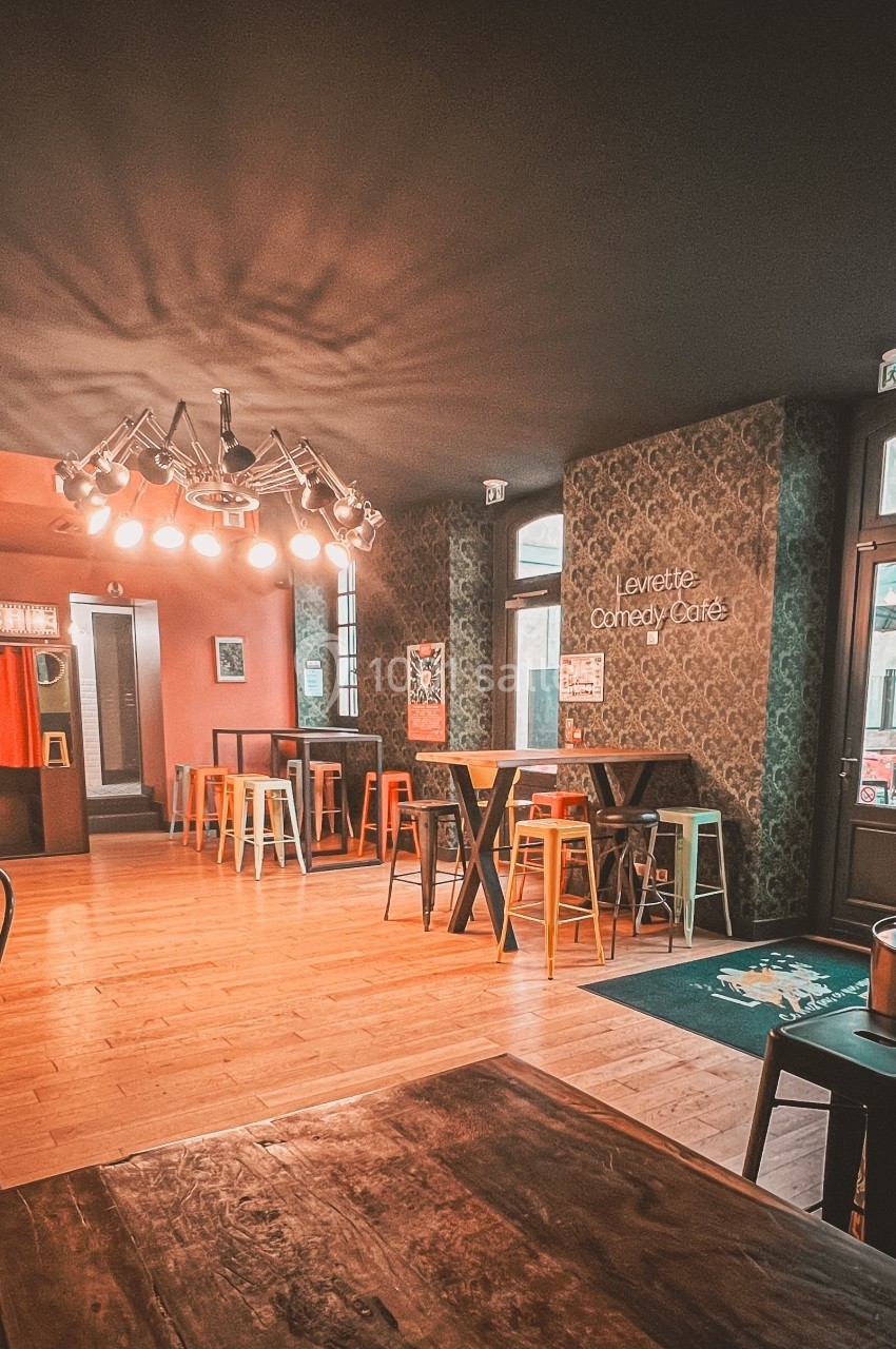 Salle de café avec tables en bois, chaises colorées et éclairage suspendu, ambiance chaleureuse et moderne.