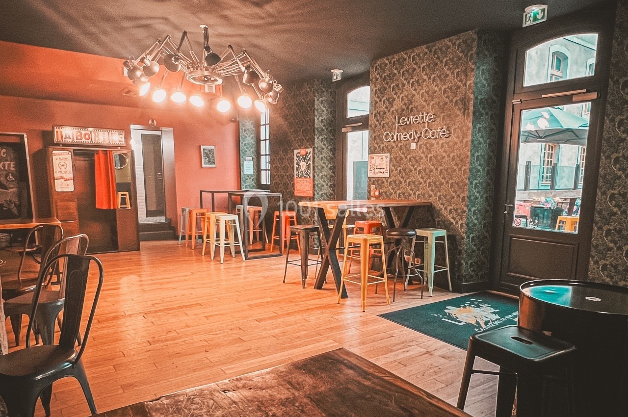 Salle de bar avec tables hautes, chaises colorées, éclairage chaleureux et décorations murales.