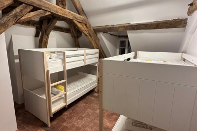Chambre avec lits superposés en bois, poutres apparentes au plafond et sol en tomettes anciennes.