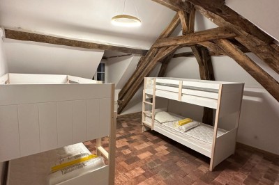 Chambre avec lits superposés en bois, poutres apparentes au plafond et sol en tomettes anciennes.