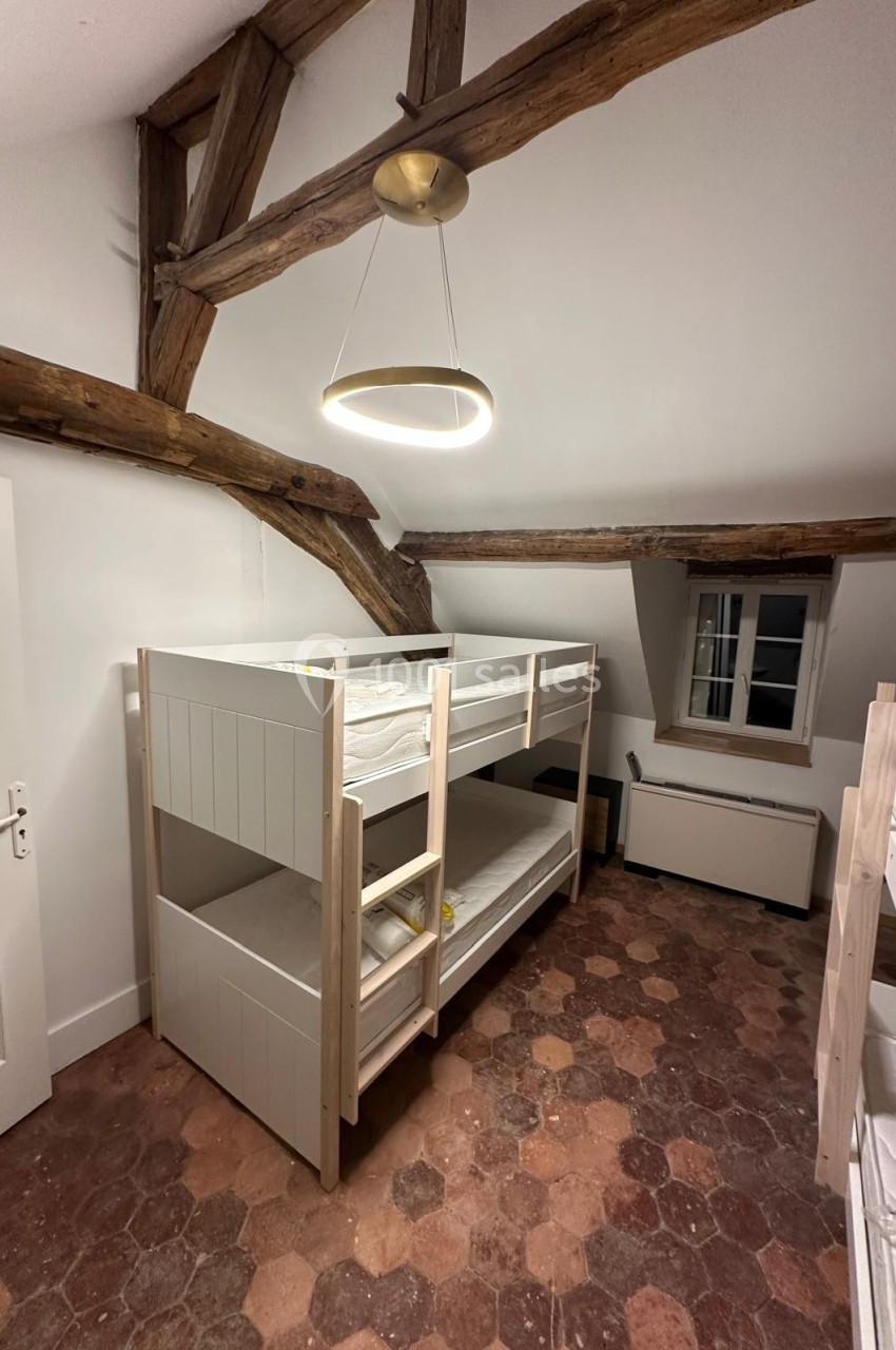 Chambre avec lits superposés en bois, poutres apparentes au plafond et sol en tomettes anciennes.