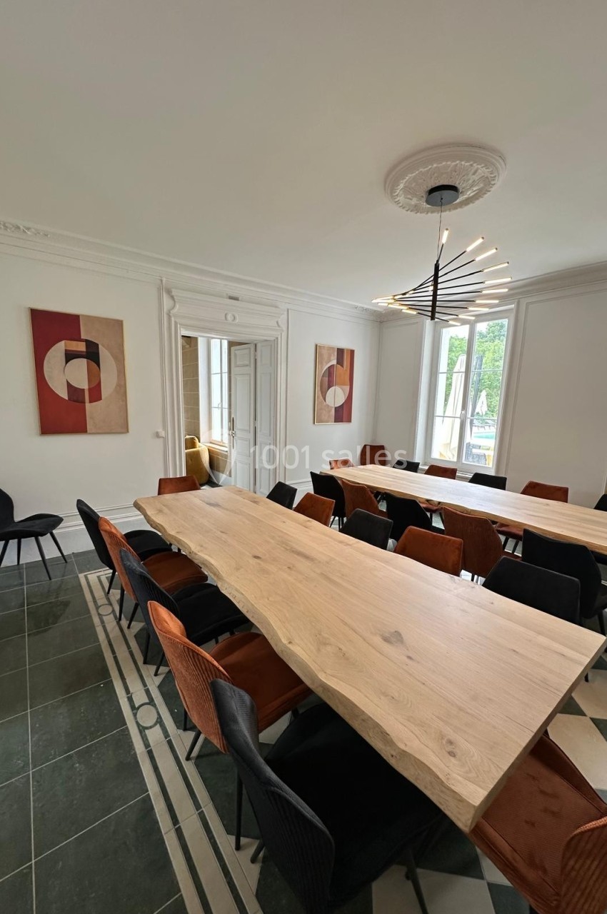 Salle de réunion lumineuse avec une grande table en bois, des chaises colorées et des œuvres d'art modernes au mur.