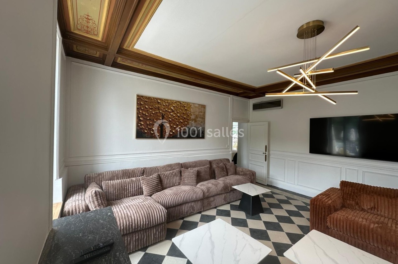 Salon élégant avec canapé en velours, tables basses en marbre, lustre moderne et plafond orné de moulures.