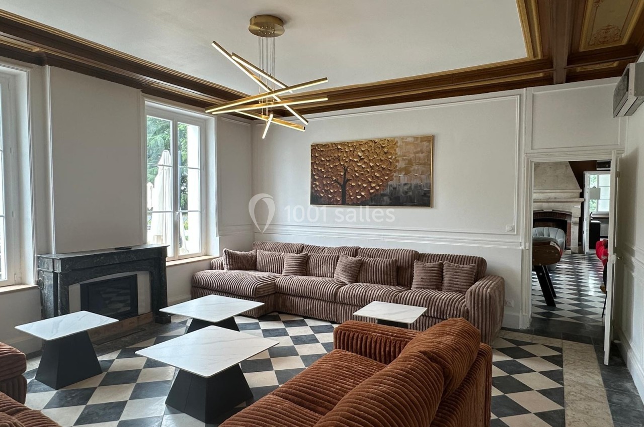 Salon lumineux avec canapés en velours marron, tables basses en marbre, cheminée et lustre moderne, sol en damier.